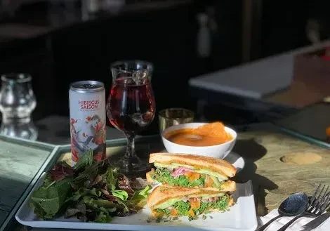 Sandwich, salad, soup, and Hibiscus Saison beer on a wooden table.