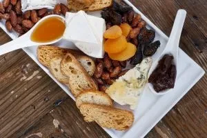 Close-up charcuterie board with cheese, crackers, almonds, dried fruit, honey, jam.