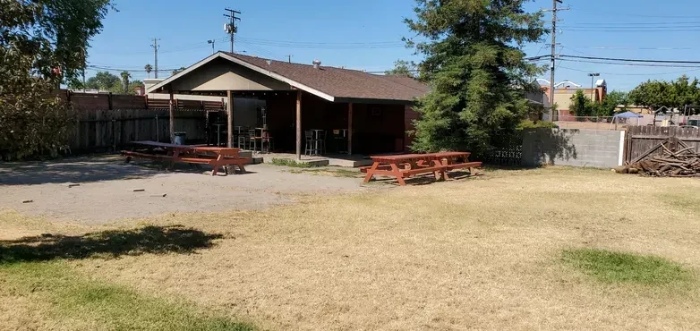 Outdoor restaurant with red picnic tables, gravel, and covered patio.