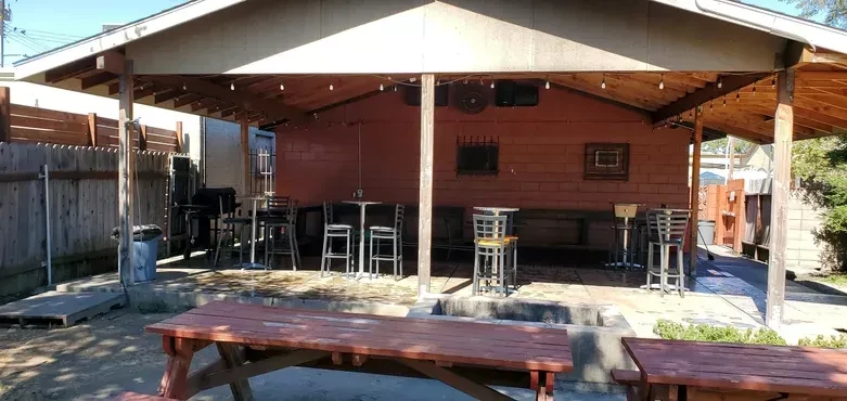 Empty outdoor patio with wooden picnic tables and covered high-top tables.