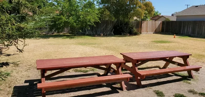 Two large wooden picnic tables on dry ground under a sunny sky.