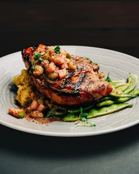 Plated grilled meat with fruit relish, mashed potatoes, and snap peas.