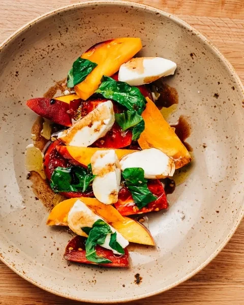 Overhead: Peach, mozzarella, basil salad with balsamic glaze in a bowl.