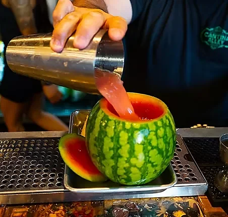 Bartender pouring red cocktail into a hollowed watermelon at the bar