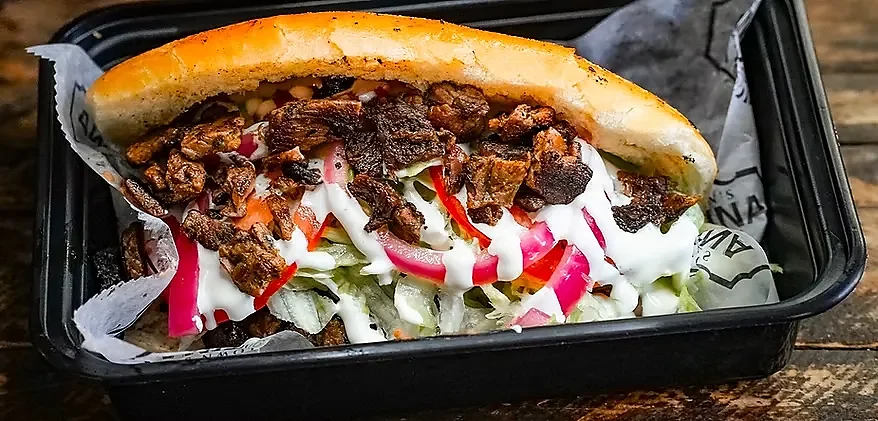 Torta with grilled meat, lettuce, pickled onion and crema in takeout container