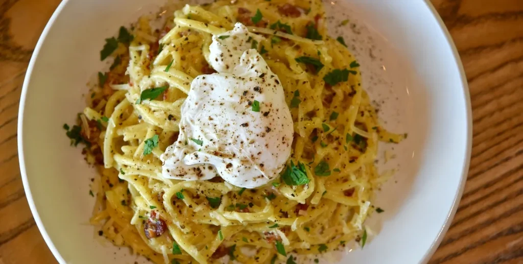 Overhead view of creamy pasta with bacon, herbs, and burrata.