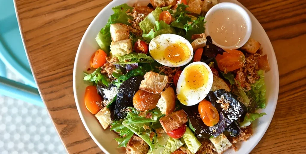 Vibrant salad with greens, tomatoes, croutons, cheese, and soft-boiled eggs.