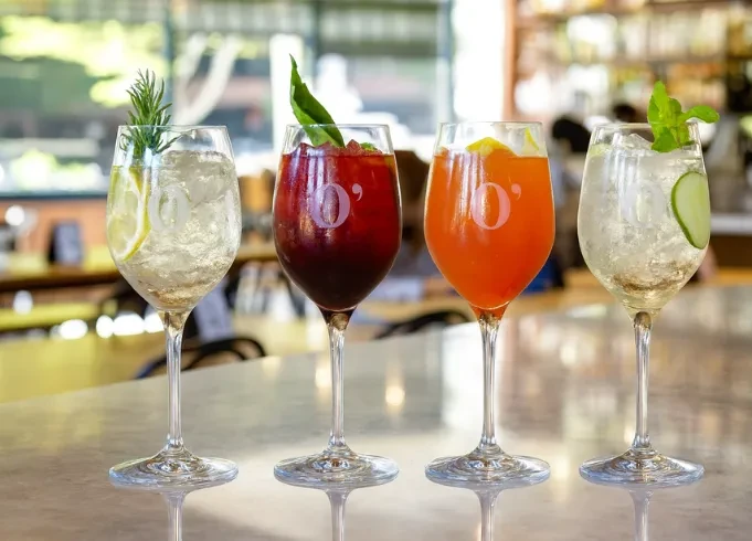 Four colorful, garnished cocktails in stemware on a reflective surface.