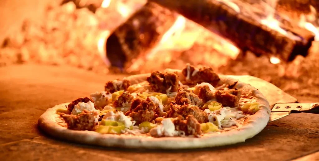 Partially baked pizza on a peel in a wood-fired oven.