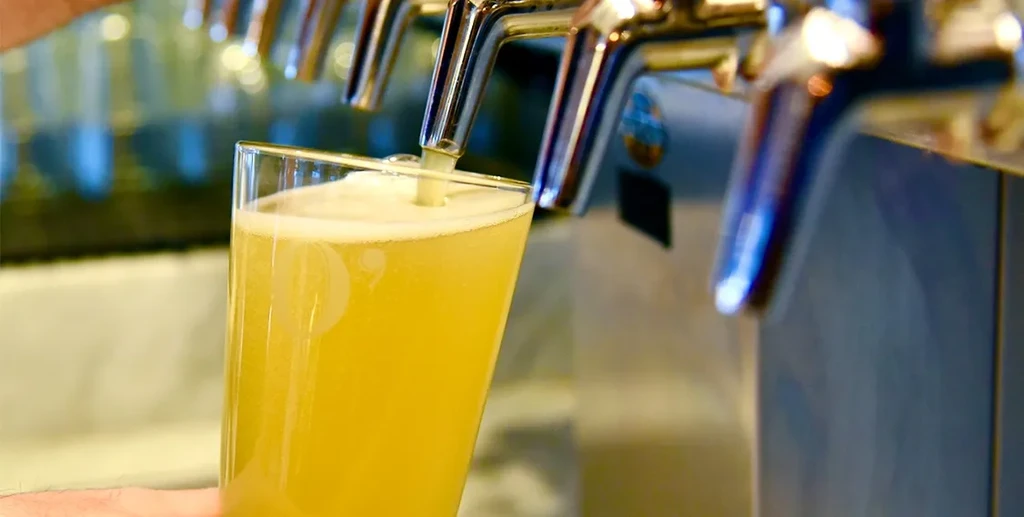 A glass fills with golden, foamy beer from a chrome tap.