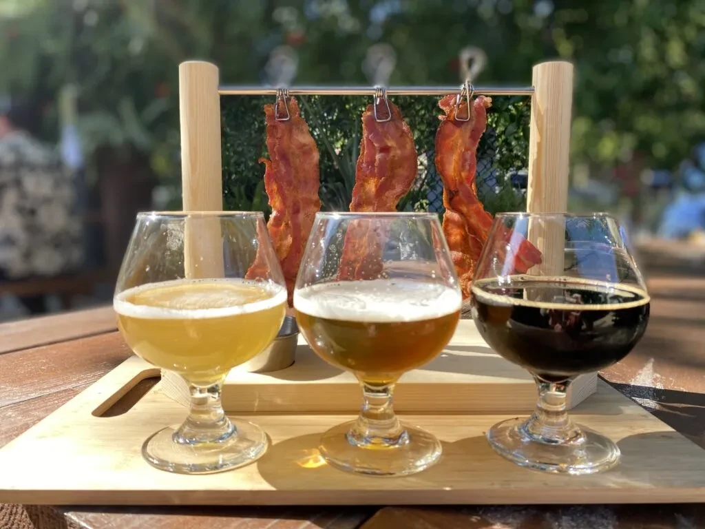 Beer flight and hanging bacon on a serving tray outdoors.