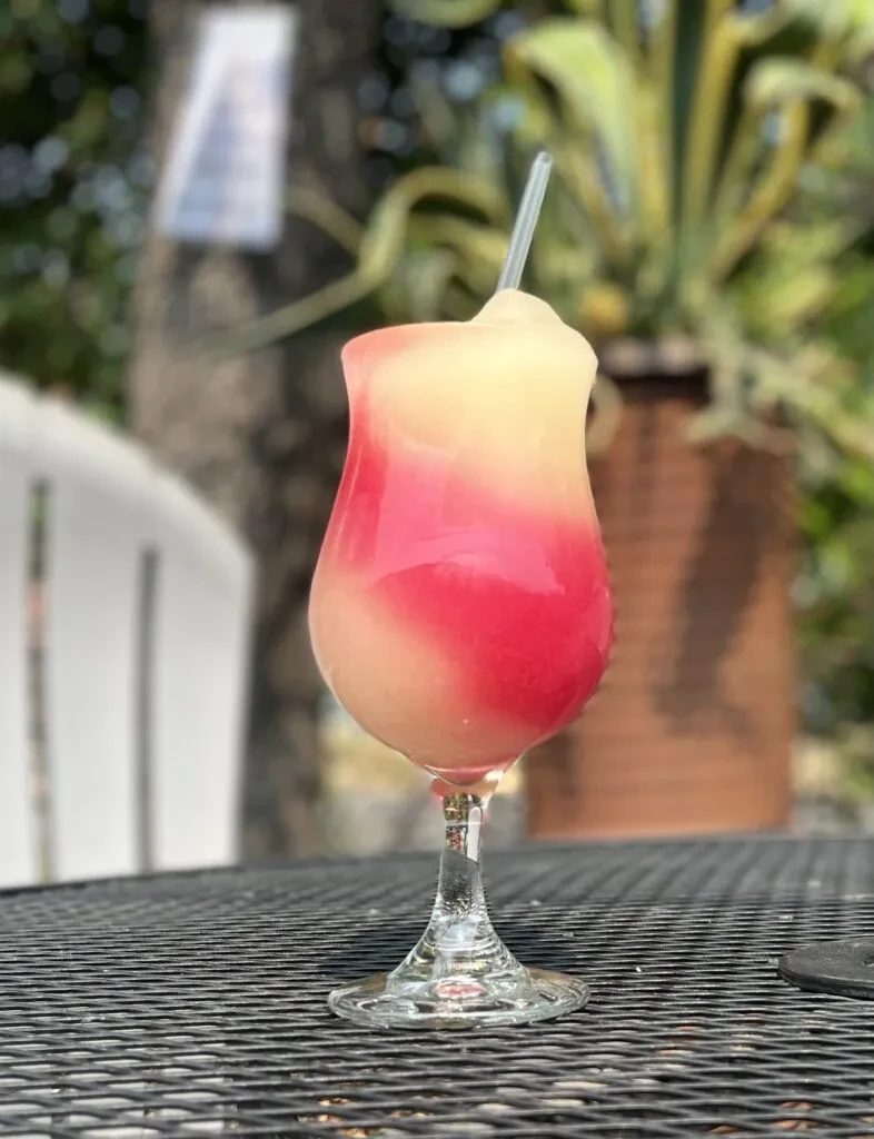 Yellow and pink layered frozen drink with straw in a stemmed glass.