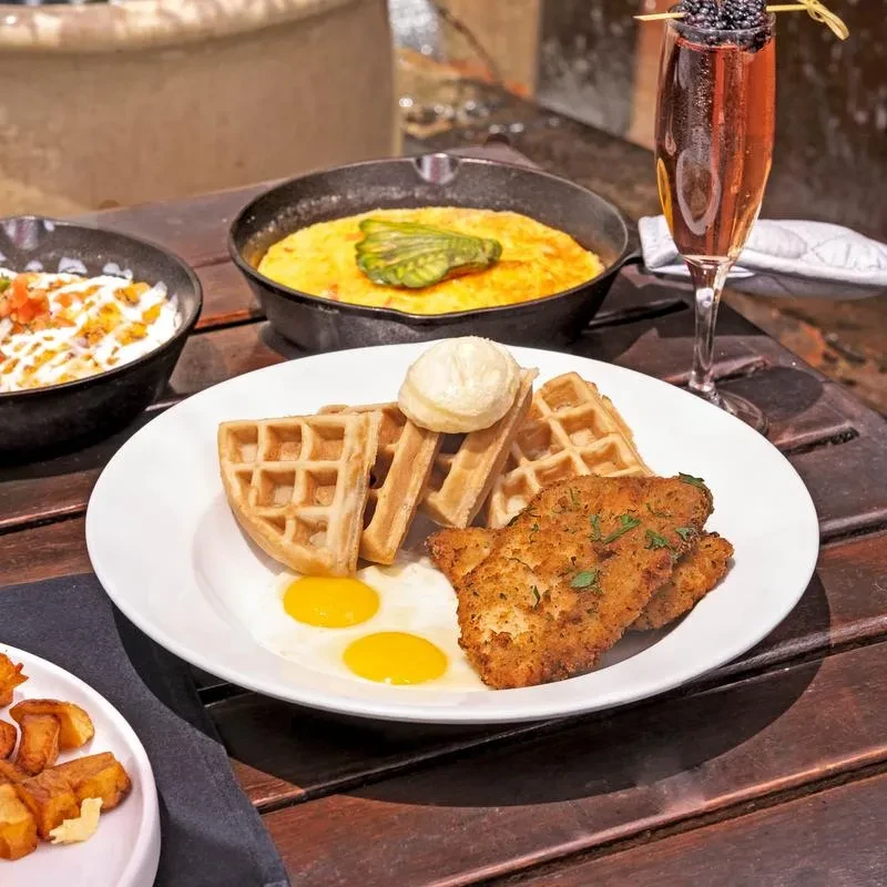 Brunch spread with waffles, fried chicken, eggs, grits, and a sparkling drink.