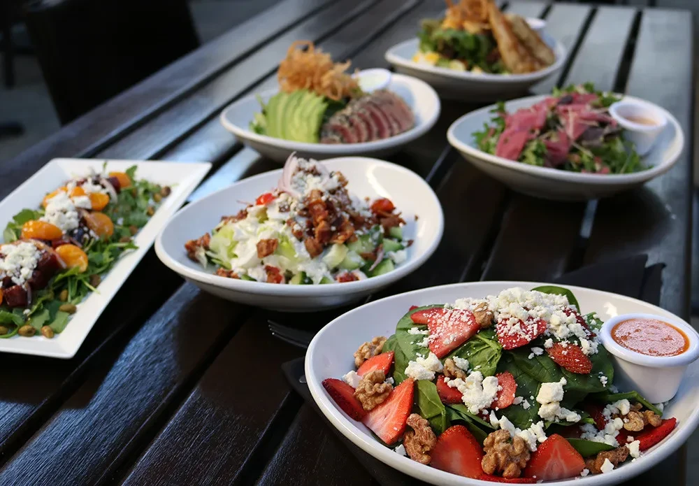 A spread of gourmet salads and dishes on a dark table outdoors.