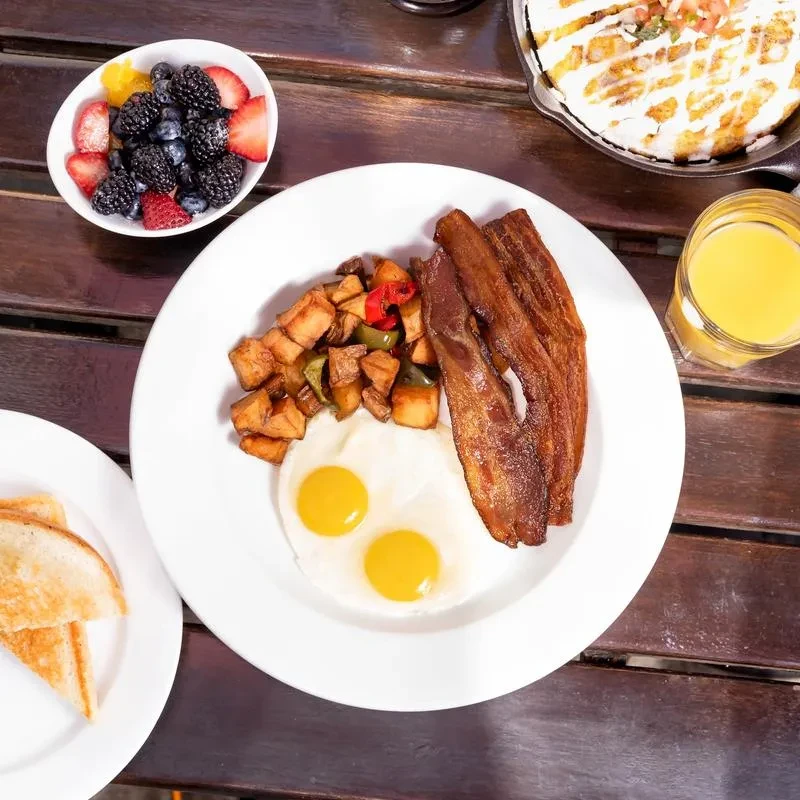 Top-down view: eggs, bacon, home fries, berries, orange juice, toast.