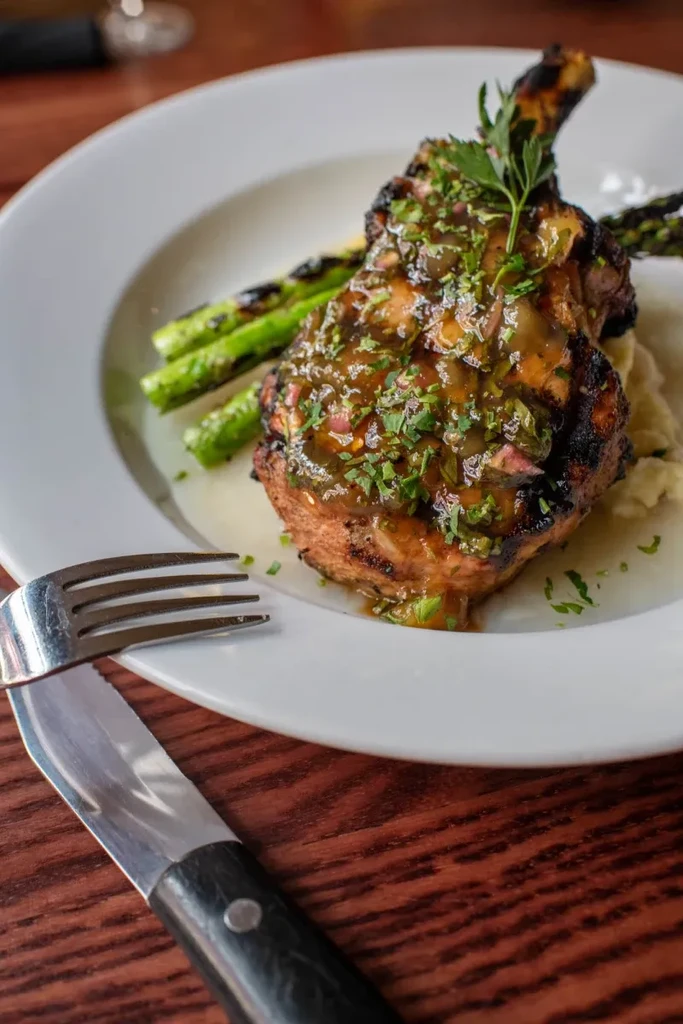 Grilled pork chop with sauce, mashed potatoes, and asparagus.