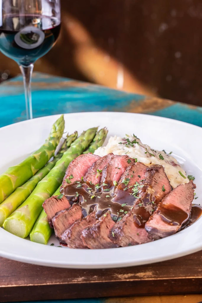 Sliced steak meal with asparagus, mashed potatoes, and red wine.