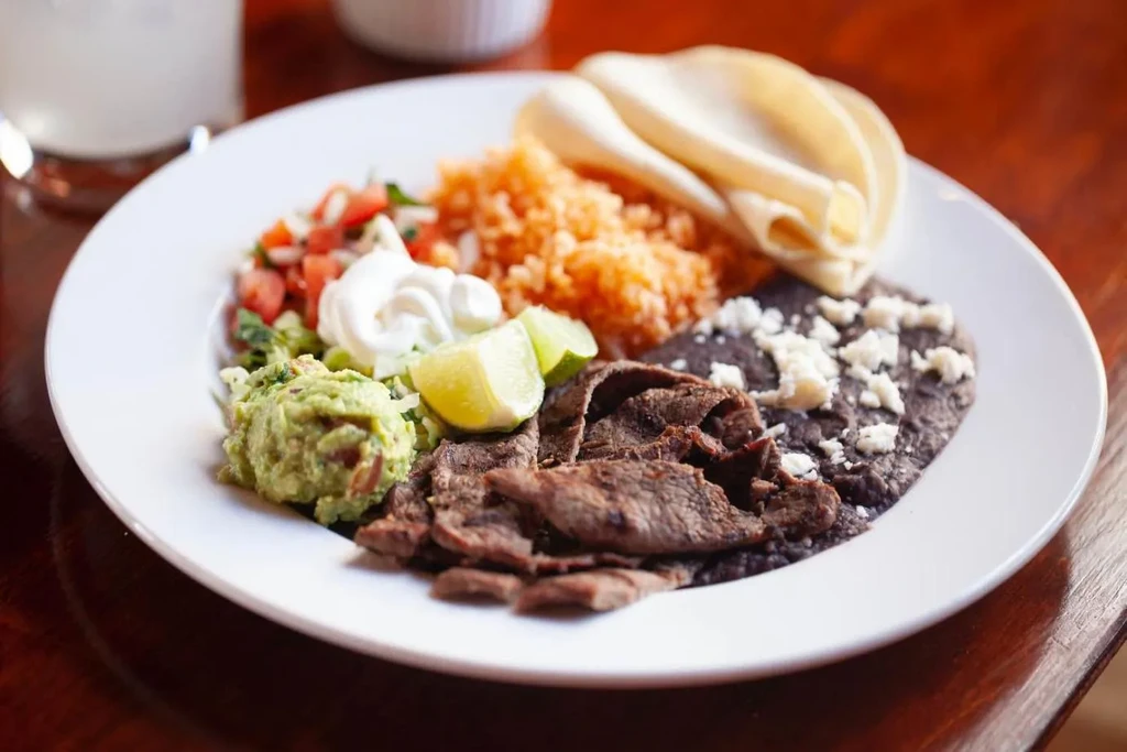 Colorful Mexican plate with grilled meat, beans, guacamole, and tortillas.