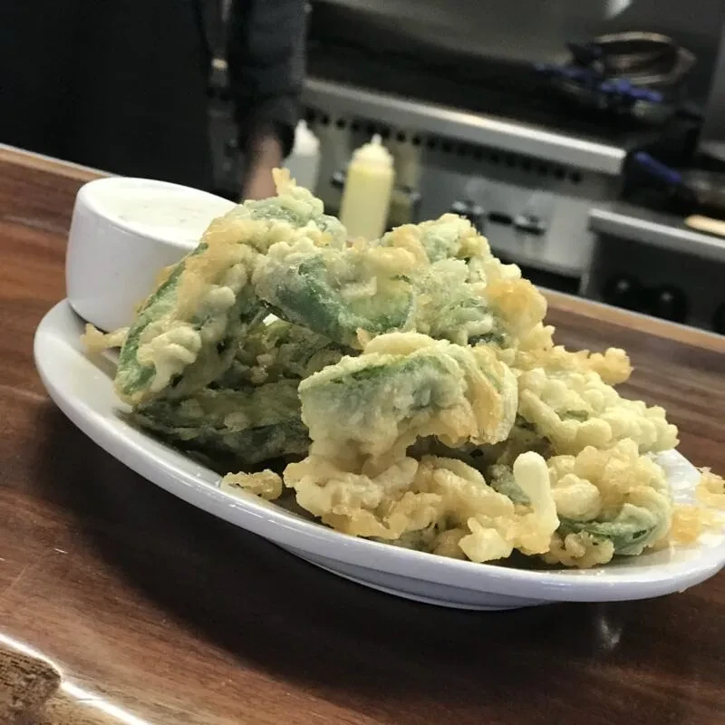 Crispy deep-fried green vegetables with creamy dipping sauce on a plate.