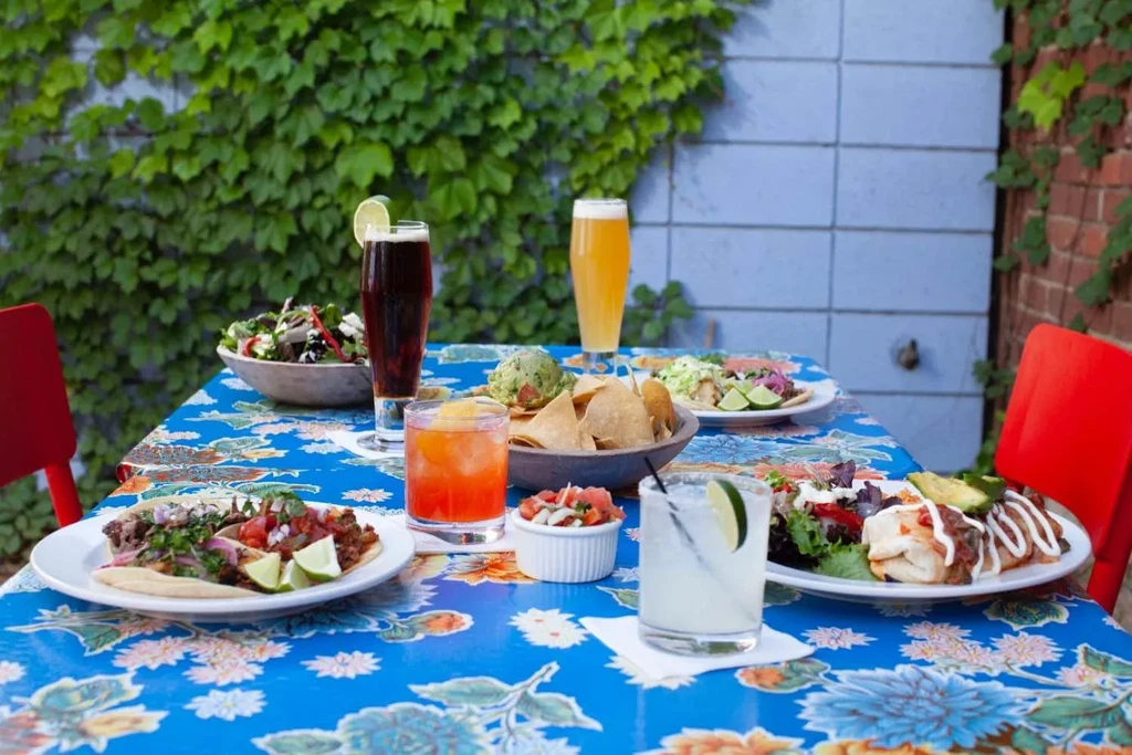 Outdoor table with blue floral tablecloth, colorful Mexican food, and drinks.