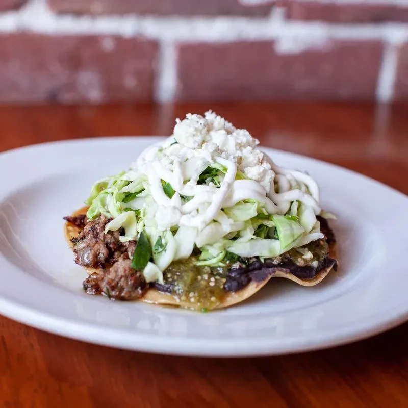Tostada topped with black beans, meat, cabbage, crema, and cheese.