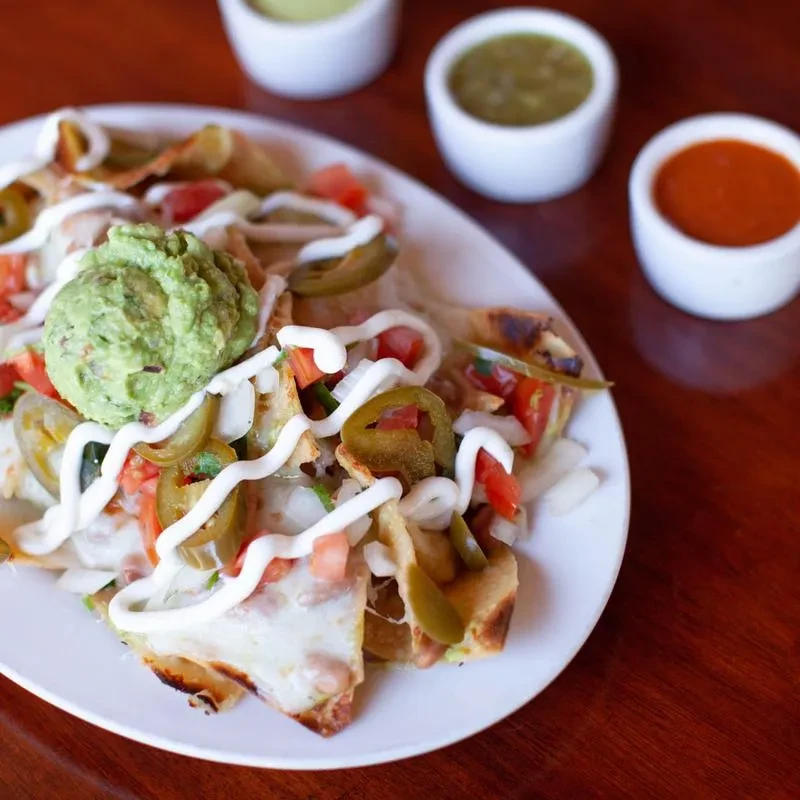Close-up of loaded nachos with cheese, guacamole, tomatoes, jalapeños, and sour cream.