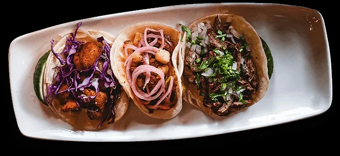 Three tacos featuring diverse fillings and colorful toppings on a white plate.