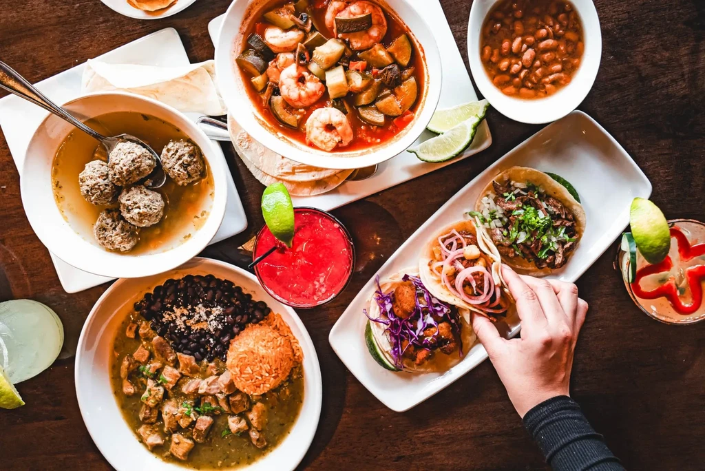 Overhead shot of various Mexican dishes: tacos, soups, stews, and drinks.
