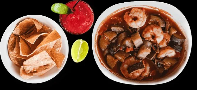 Tortilla chips, red drink, lime, and shrimp stew on black.