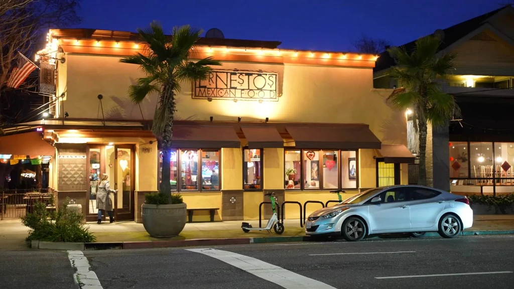 Brightly lit Ernestos Mexican Food exterior with palm trees at night.