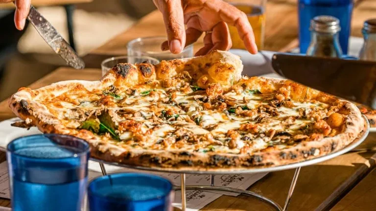 Hand lifting a slice of pizza with cheese, mushrooms, and sausage.