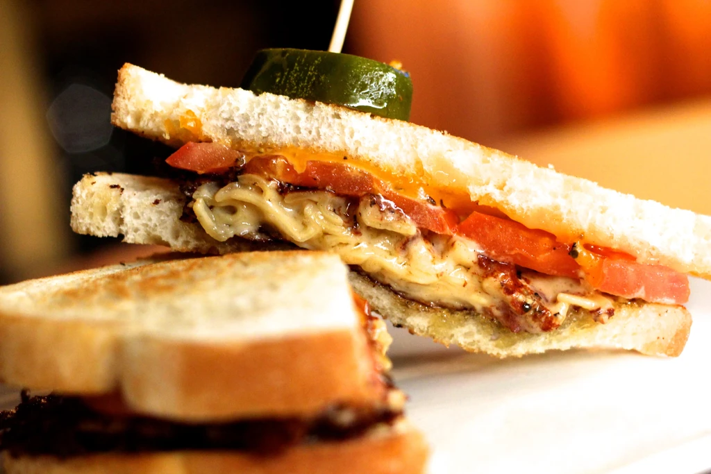 Halved sandwich on toasted bread with melted cheese, tomato, meat, pickle.