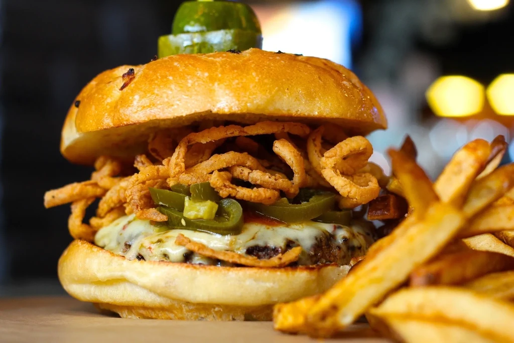 Gourmet burger with cheese, jalapeños, onion strings, pickle spear, and fries.
