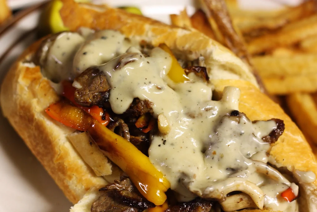 Close-up of a generously filled cheesesteak sandwich with peppers and fries.