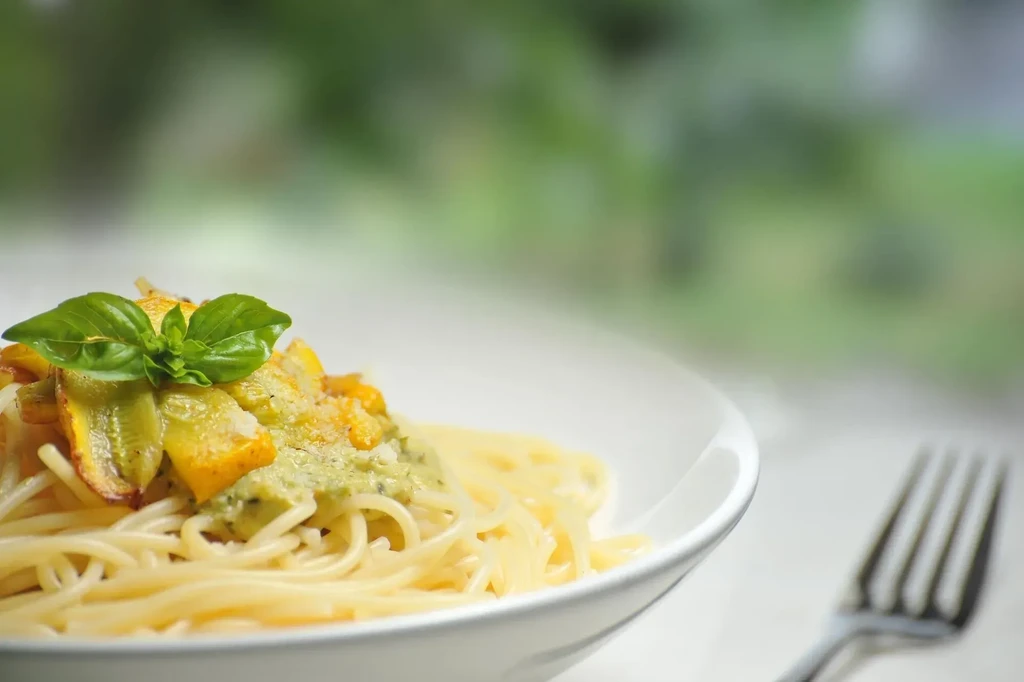 Spaghetti with yellow vegetables, green pesto, cheese, and basil sprig.