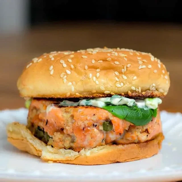 Salmon burger with toasted bun, greens, and creamy green sauce.
