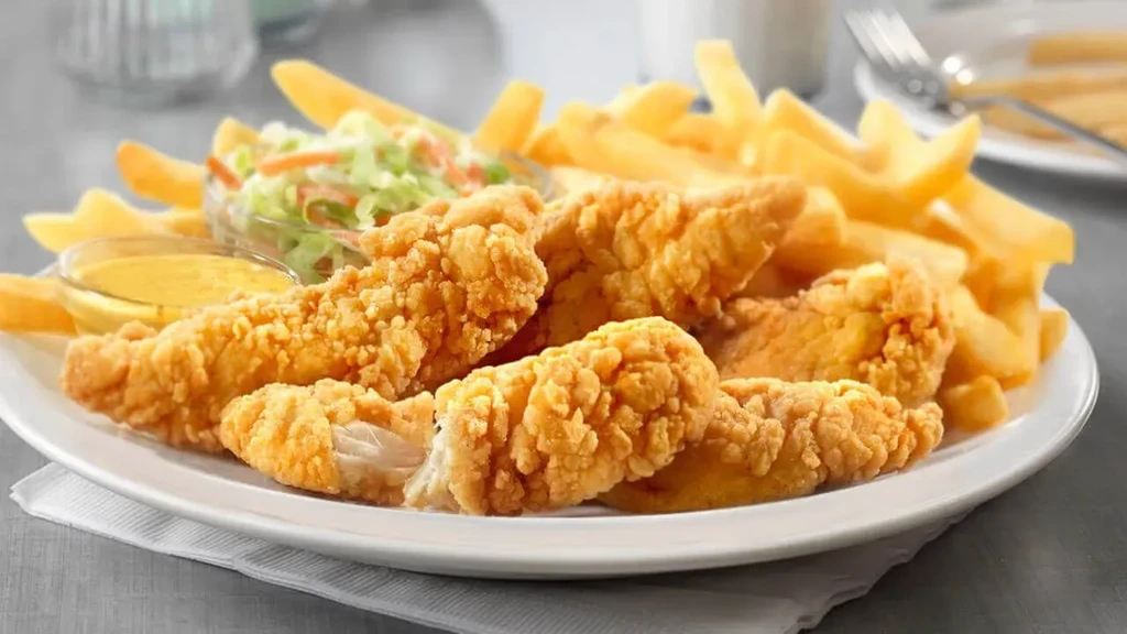 White plate with crispy chicken tenders, thick fries, dipping sauce, and coleslaw.