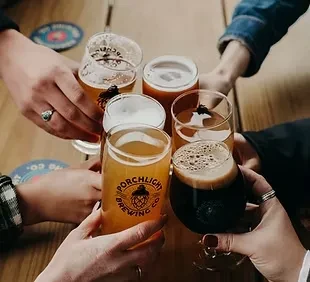 Six hands clinking diverse beer glasses, one branded Porchlight.