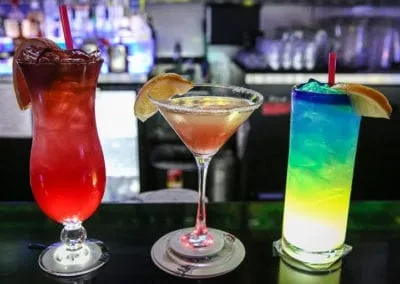 Three colorful cocktails: red, orange, and blue-green, on a bar.