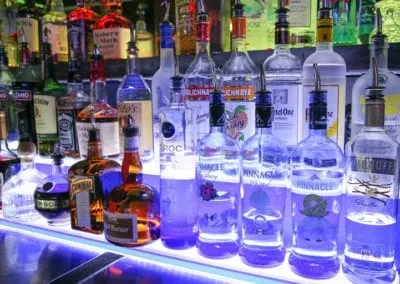 Numerous liquor bottles on a bar shelf, glowing with blue LED light.