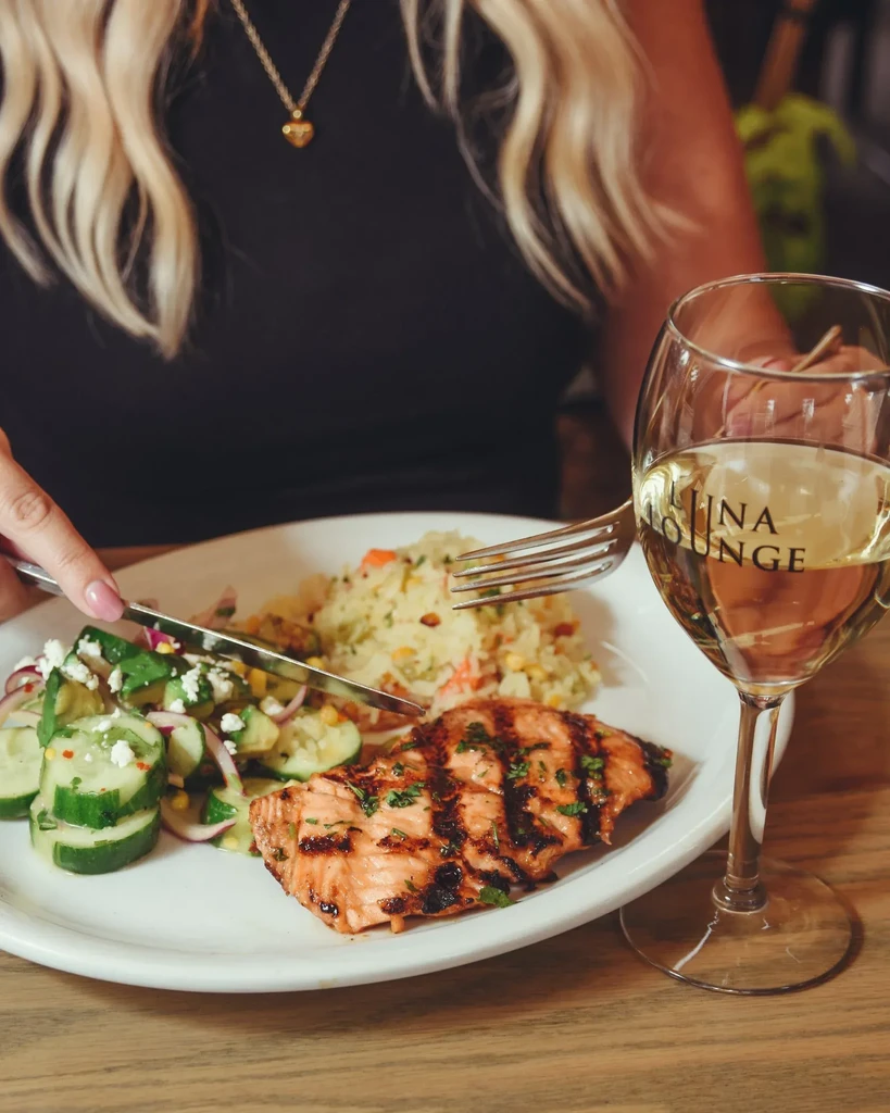 Grilled salmon meal with rice, salad, and wine glass.