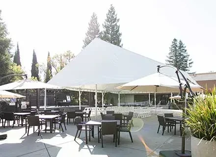 Large white tent, rows of chairs, outdoor tables, and umbrellas.