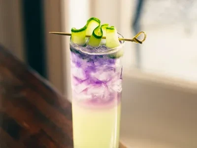 Layered purple and yellow drink with crushed ice and cucumber garnish.