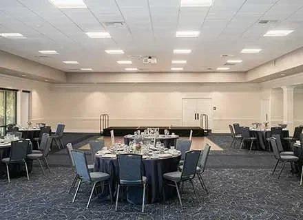 Formal, empty banquet hall prepared with dark tables and a stage.
