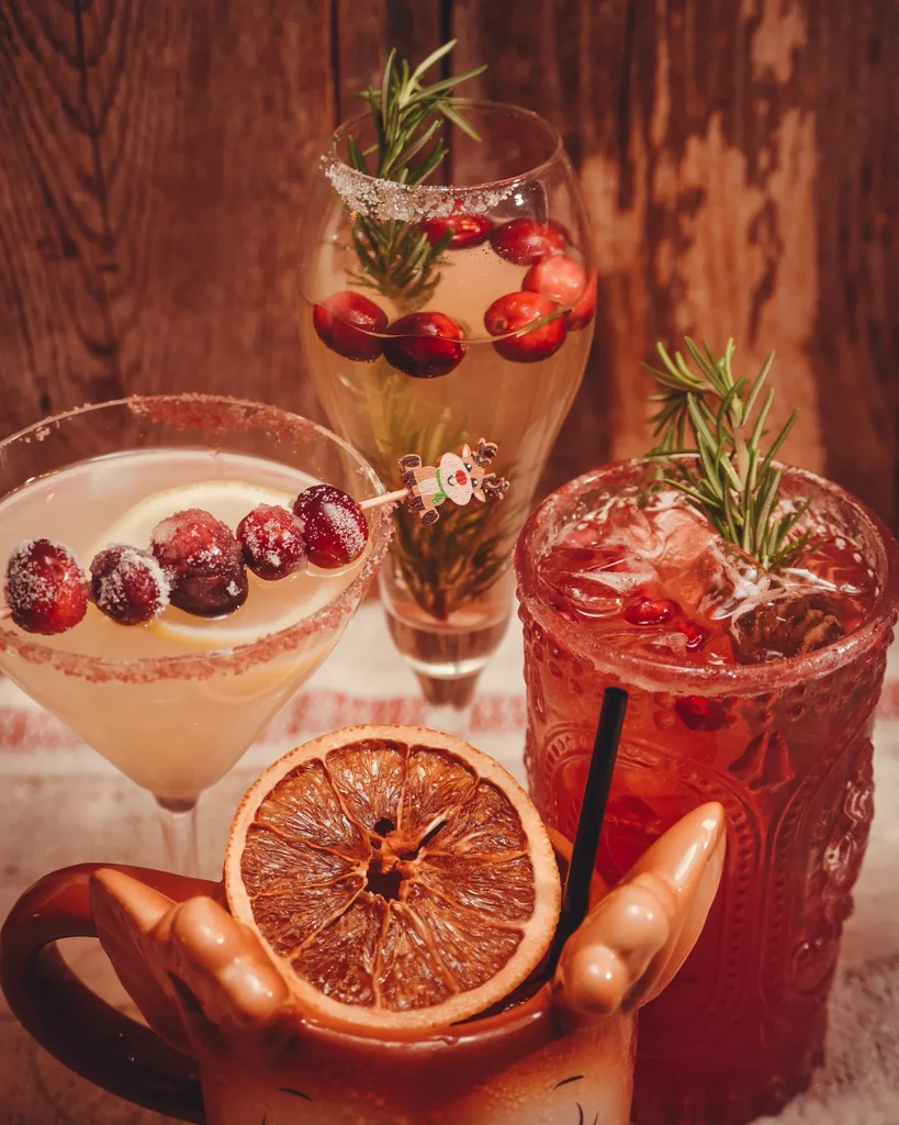 Four festive holiday cocktails with garnishes on rustic wood.