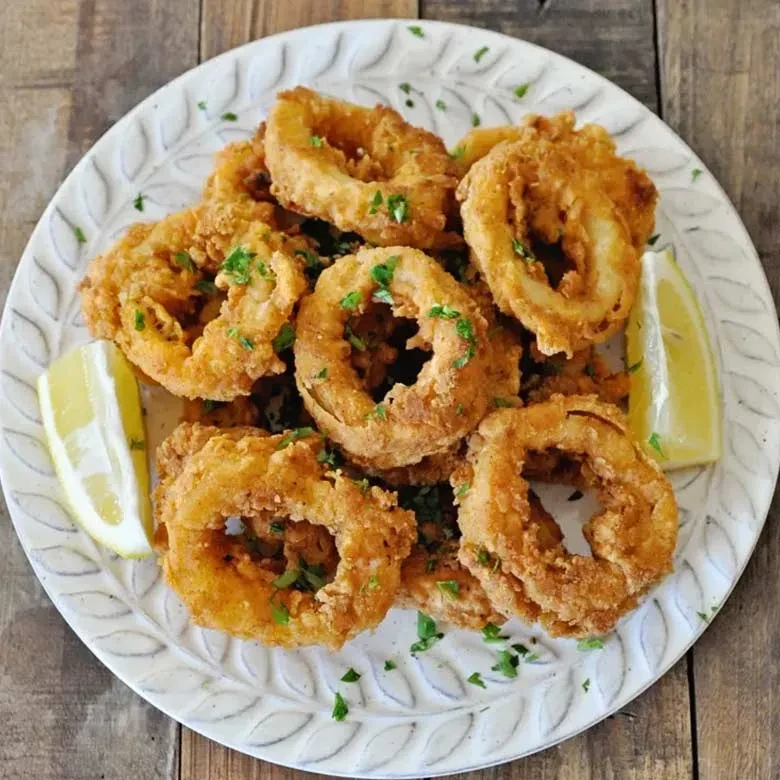 Golden-brown fried calamari rings with lemon and herbs on a white plate.
