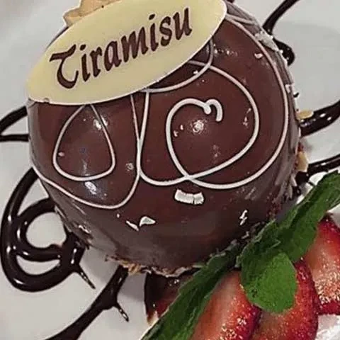 Dark chocolate Tiramisu sphere with white icing, strawberries, and mint.