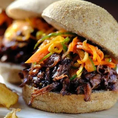 Pulled-meat sandwich with carrots and greens on a rustic whole-grain bun.