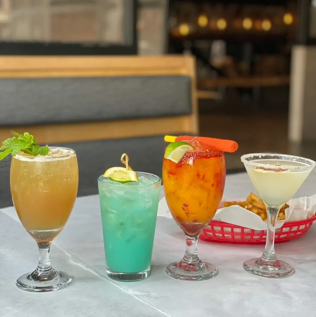 Four colorful cocktails and fries on a restaurant table.