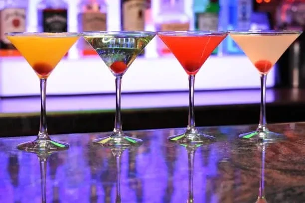 Four colorful martini cocktails with cherries on a reflective bar.